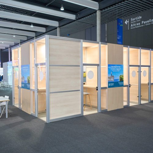 Cabinas telefónicas individuales en madera clara con estructura metálica en la zona auxiliar de EULAR 2025.