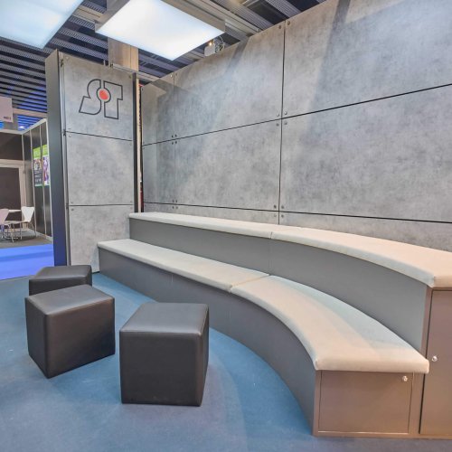 Área con graderío curvo y asientos en el stand de Servitron, diseñada para presentaciones o encuentros relajados con visitantes.